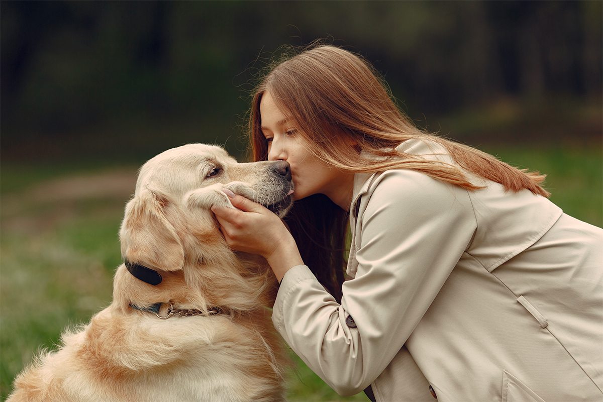 אישה עומדת בשפיפה ומנשקת על האף כלב מגזע גולדן רטריבר.